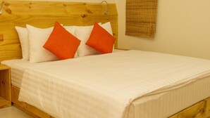 Ein hölzernes Bett mit weißen und orangefarbenen Kissen, einer weißen Bettdecke und einem Holz-Kopfteil.
