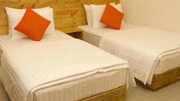 Dos camas individuales con ropa de cama blanca y almohadas naranjas, cabeceros de madera y una pared lisa.