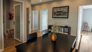 Un espace repas moderne avec une table en bois foncé, un vase rempli de fleurs et un tableau représentant un pont accroché au mur.