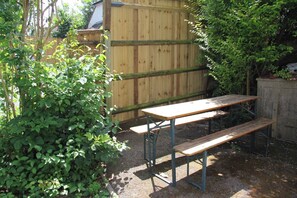A wooden table and bench set in a garden with a wooden fence and lush greenery. - Woodlands Cozy Cottage in Gerrards Cross, Sleeps 2 (Gerrards Cross)
