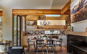 Une cuisine moderne avec des poutres en bois, des meubles blancs et un coin repas agrémenté d’un tapis à motifs.