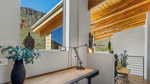 Una habitación moderna con un escritorio de madera, un ventanal con vistas a la montaña, una planta de cactus y una silla.