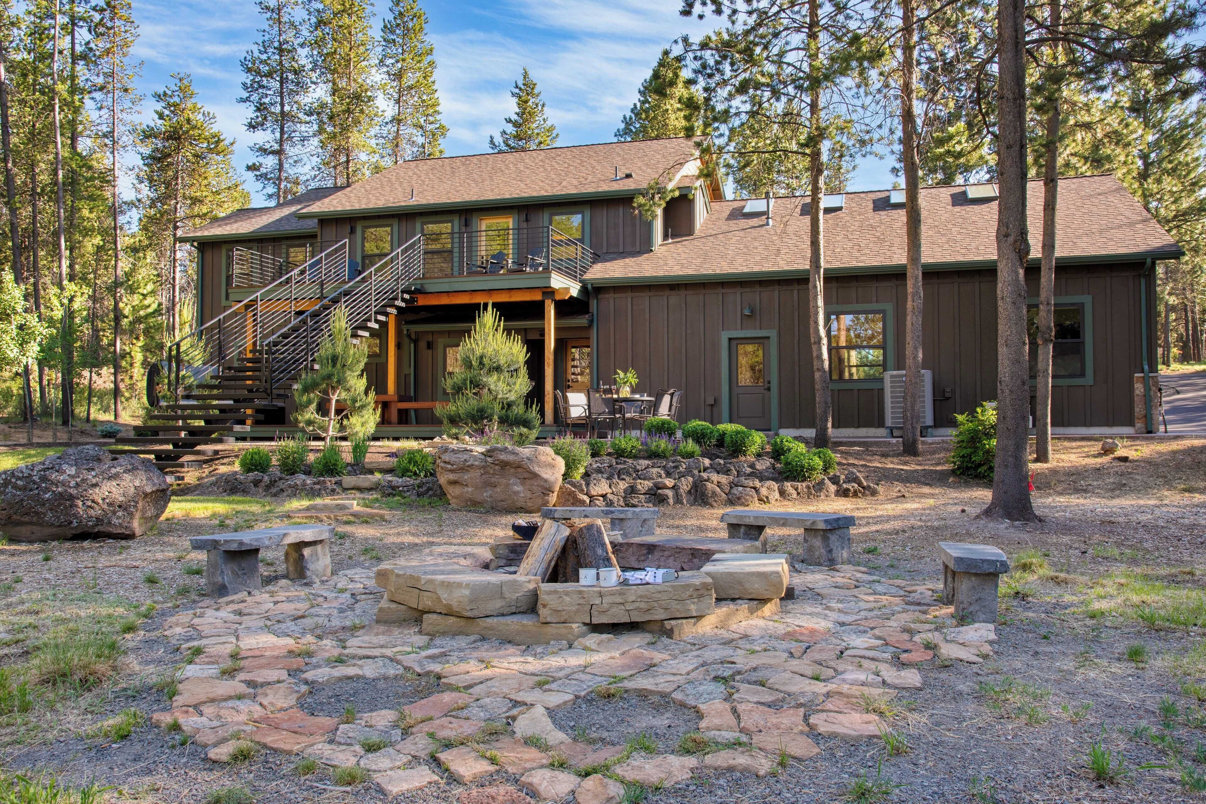 A two-story lodge with a stone fire pit, outdoor seating, and a staircase leading to a deck.