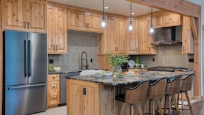 Een moderne keuken met houten kastjes, een roestvrijstalen koelkast, een marmeren eiland en barstoelen.