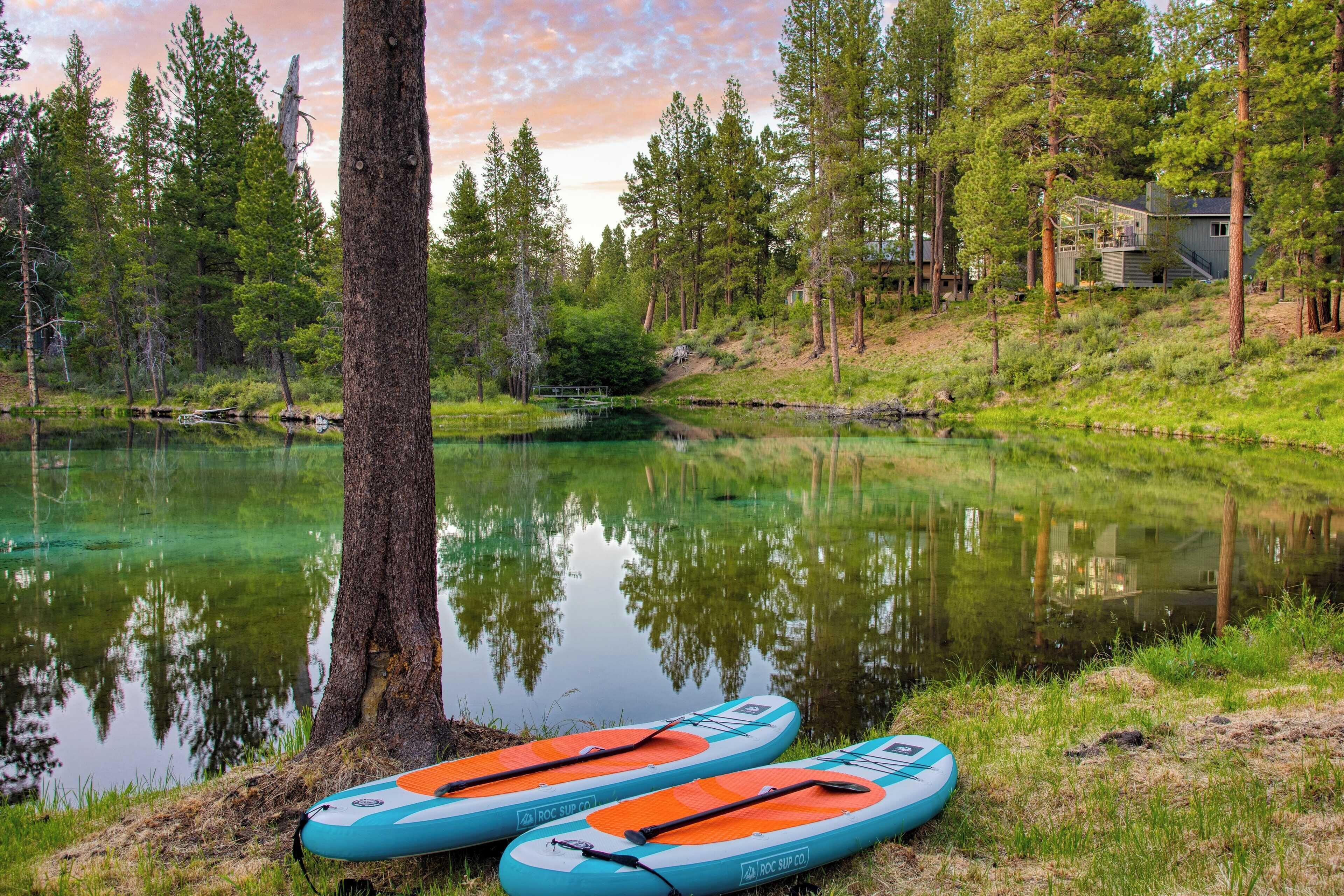 Two paddleboards by a calm lake with a house in the background.