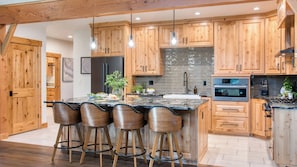 Una cocina moderna con armarios de madera, una isla central con taburetes de bar, un horno Bosch y un refrigerador de acero inoxidable.