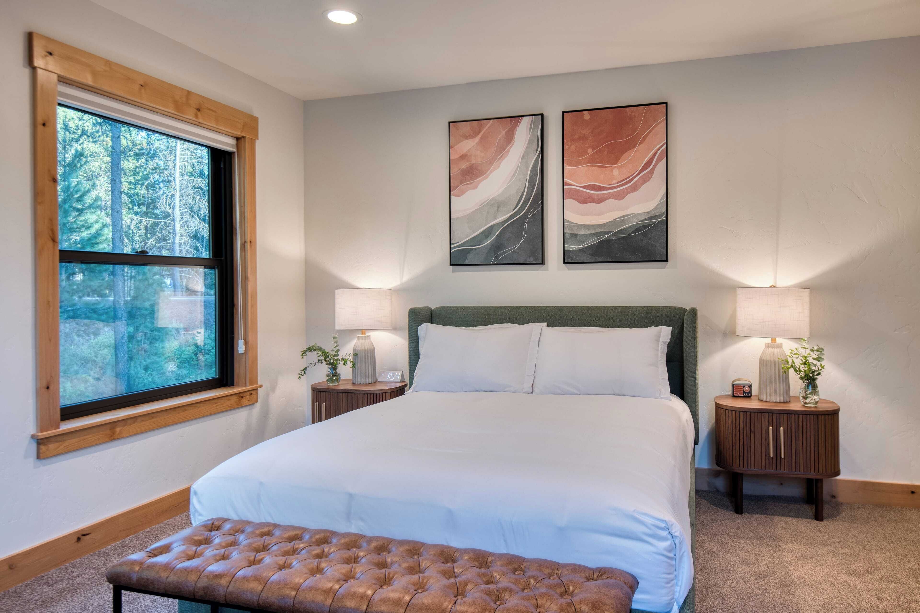 Une chambre à coucher avec un grand lit, deux tables de chevet, une fenêtre et des œuvres d’art abstraites accrochées au mur.