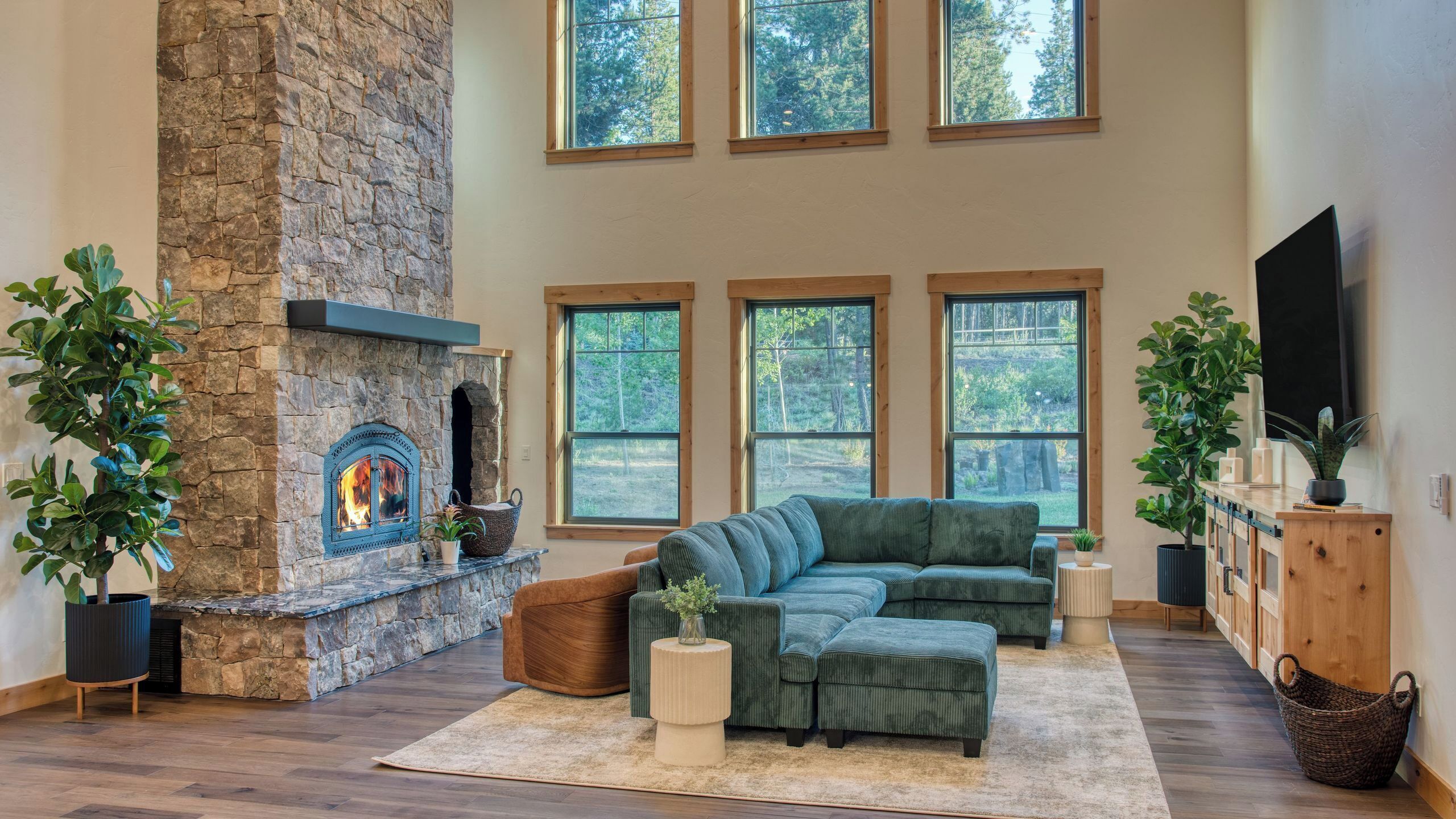 A spacious living room with a stone fireplace, large windows, a sectional sofa, and a flat-screen TV.