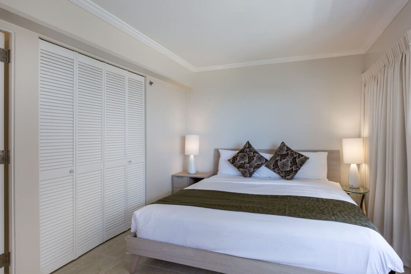 A hotel room with a bed, two bedside lamps, a nightstand, and a wardrobe.