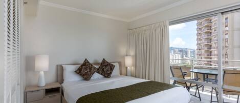 Una habitación de hotel con una cama grande, dos lámparas de noche, una mesita de noche, un plaid verde y un balcón con mesa y sillas.