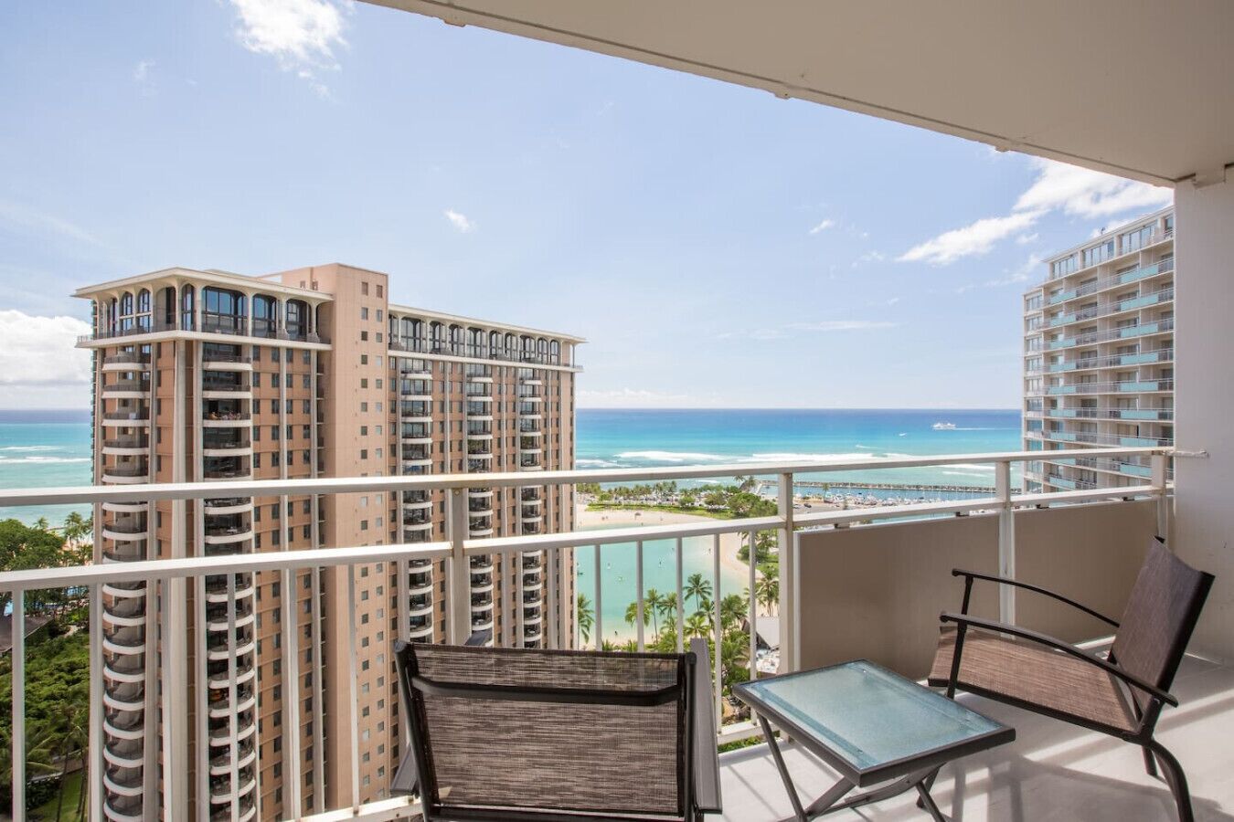 A balcony with two chairs and a table overlooking a beach and high-rise buildings.