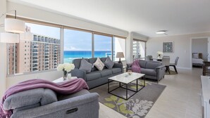 Ein modernes Wohnzimmer mit großem Fenster, grauen Sofas, einem Couchtisch und Blick auf den Ozean.