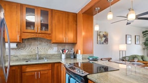 Une cuisine moderne avec des meubles en bois, un plan de travail en granit, une cuisinière et un ventilateur de plafond.