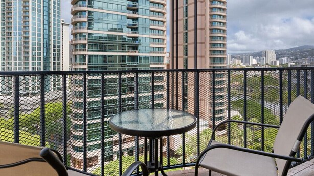 Un balcon avec une table et des chaises en verre, donnant sur un paysage urbain avec de hauts immeubles.