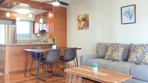 Une cuisine moderne avec un coin repas, un ventilateur de plafond et un canapé gris agrémenté de coussins à motifs.