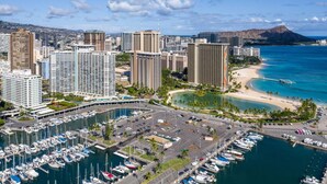 A marina with numerous boats, a coastal cityscape with high-rise buildings, and a beach with clear blue waters. - 16 FREE Parking/Ocean 1b Waikiki (Honolulu)