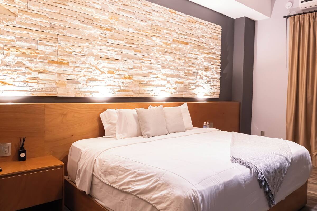 Habitación de hotel con una cama grande, cabecero de madera y una pared de piedra.