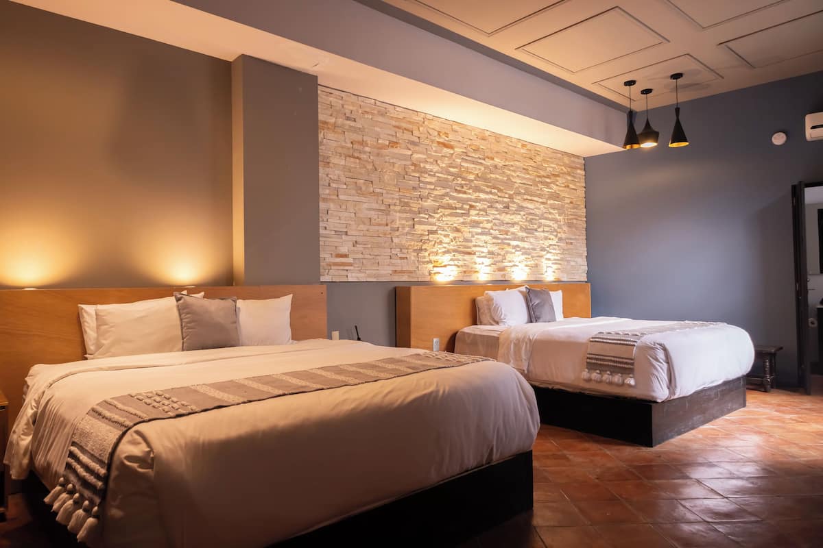Habitación de hotel con dos camas, una pared de piedra e iluminación colgante.