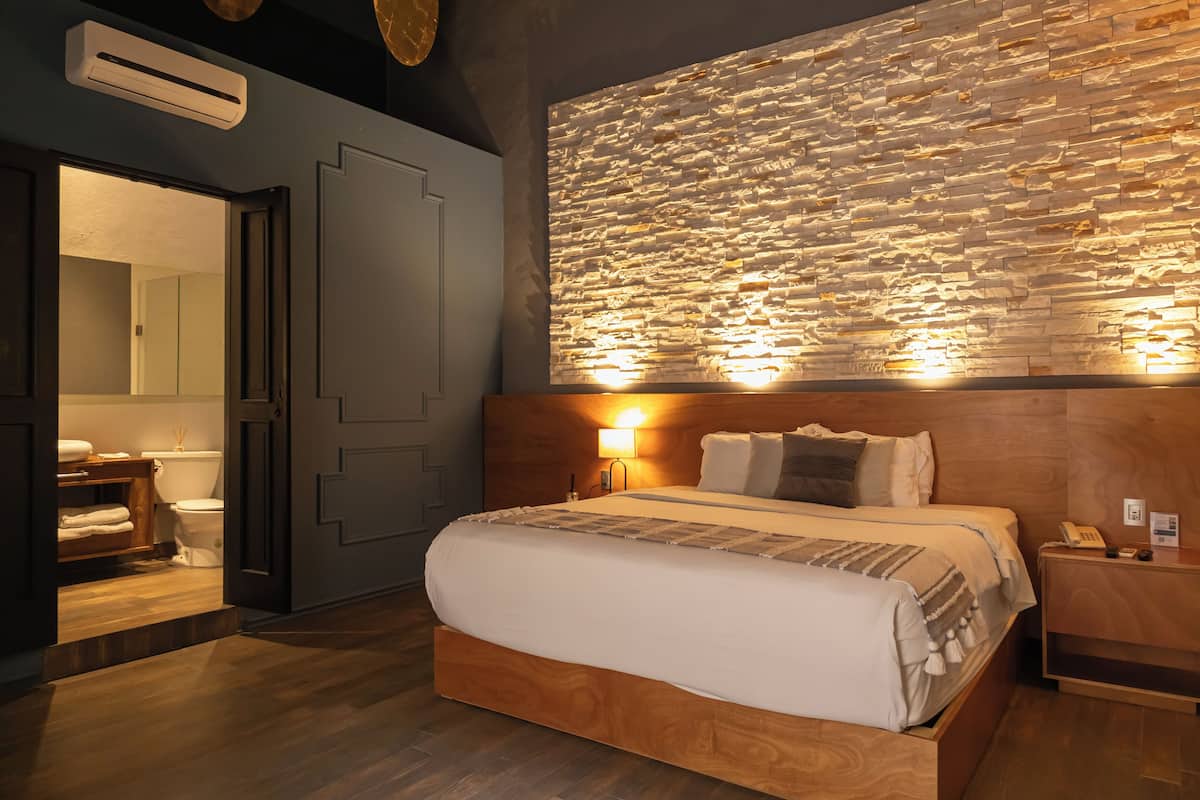 Una habitación de hotel moderna con una cama grande, cabecero de madera y un revestimiento de pared con textura.
