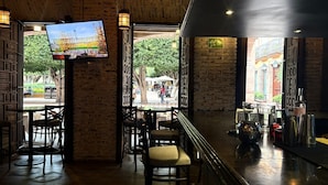 Un interior con paredes de ladrillo, un televisor montado en la pared y una zona de bar con taburetes y mostrador.