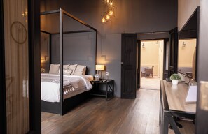Une chambre à coucher avec un lit à baldaquin, des tables de chevet, un bureau avec une chaise et une petite plante en pot.