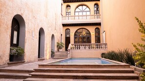 Un patio con piscina, escaleras que conducen a un edificio con ventanales arqueados y un balcón.