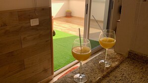 A balcony with a view of the sea, two glasses of orange juice on a granite countertop, and a small potted plant.