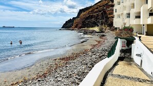 A coastal hotel with a rocky beach, clear blue sky, and a large ship in the distance.