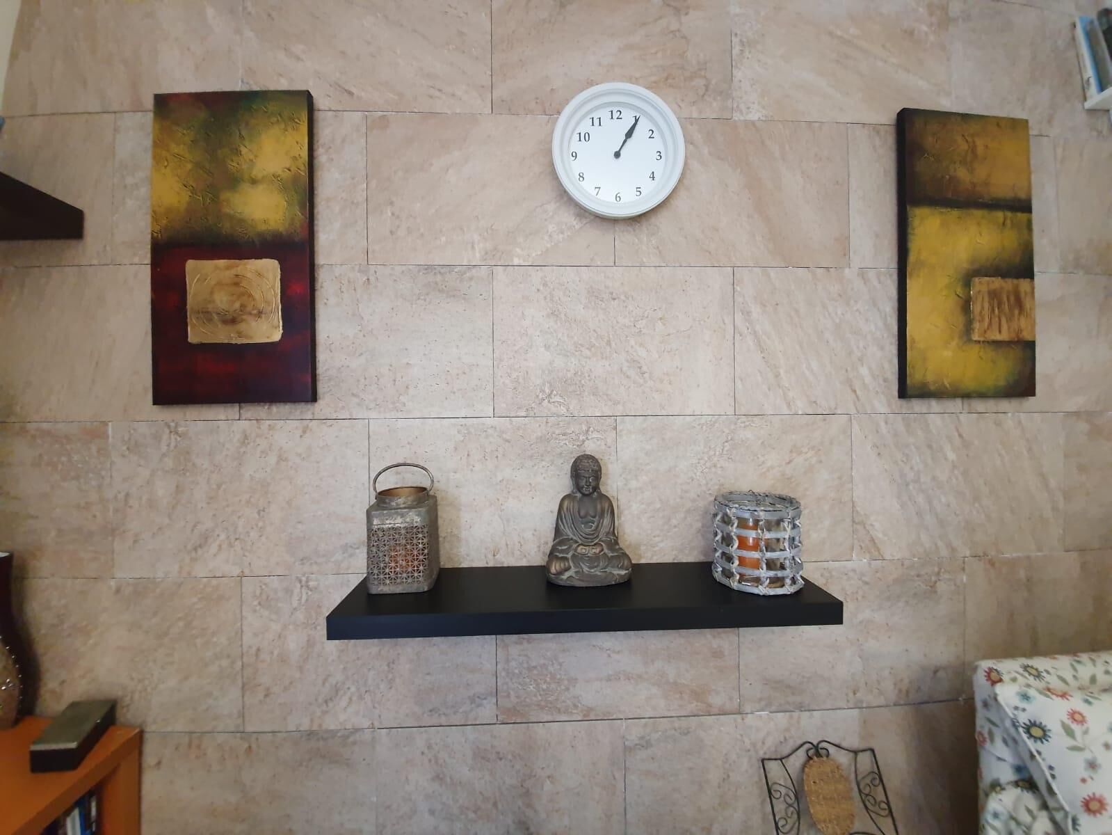 Una pared con un reloj, dos cuadros abstractos y una estantería con adornos.
