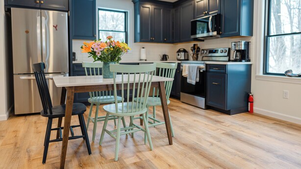 A modern kitchen with dark blue cabinets, stainless steel appliances, and a wooden dining table with chairs. - Downtown Freeport Barn'acle (Freeport)