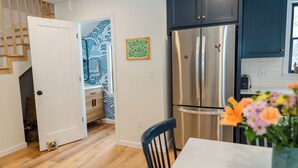 A modern kitchen with a stainless steel refrigerator, wooden flooring, and a dining area with a table and chairs. - Downtown Freeport Barn'acle (Freeport)