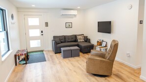 A modern living room with a grey sectional sofa, a brown armchair, and a small side table with a basket and picture frame. - Downtown Freeport Barn'acle (Freeport)