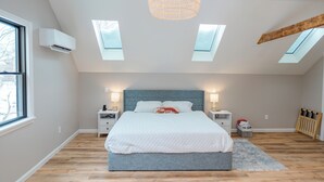 A bedroom with a large bed, skylights, a wooden ceiling beam, and a window. - Downtown Freeport Barn'acle (Freeport)