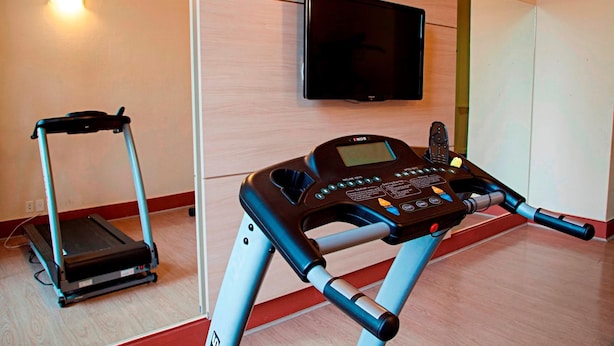 A treadmill and a stationary bike in a room with a television mounted on the wall. - Pousada Bom Jesus (Aparecida)
