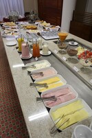 Un bufé con diversos alimentos y bebidas, incluyendo bandejas de carnes frías, quesos y frutas, además de una selección de zumos y batidos.