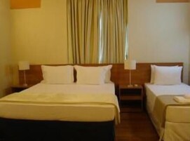 Una habitación de hotel con una cama grande, dos camas más pequeñas, una mesita de noche con lámpara y una ventana con cortinas.