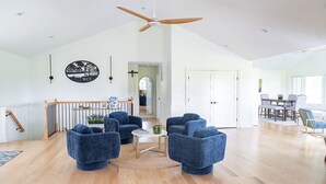 Een ruime woonkamer met een hoge plafond en een houten plafondventilator, plus een eethoek met een tafel en stoelen.