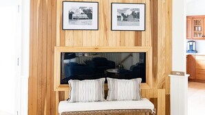 Een kamer met een houten paneel, een bank met gestreepte kussens en twee zwart-wit foto's in lijsten.