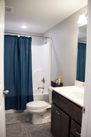 Un baño con inodoro blanco, bañera, cortina de ducha, lavabo y un armario.