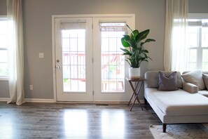 Una sala de estar con un sofá color crema, una planta en maceta y un ventanal corredizo que da a un espacio exterior.