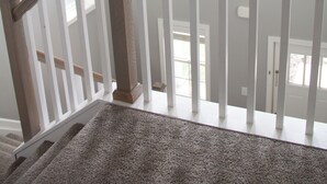 Un escalier doté d’une rampe en bois et de balustrades blanches, menant à un palier où est suspendu un luminaire.