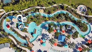 Een vogelperspectief van een resort met kronkelende zwembaden, palmbomen en ligbedden.