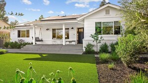 Een modern wit huis met een overdekte veranda, een verzorgd gazon en diverse planten.