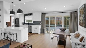 Een moderne keuken met een centraal eiland, een eethoek met tafel en stoelen, en een grote glazen schuifdeur naar een terras.