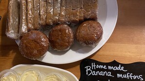 Un plato de muffins de plátano caseros y pan de plátano, junto con un letrero que indica que fueron hechos por el anfitrión.