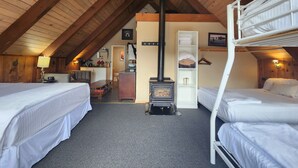 Un dormitorio abrigado en el ático con dos camas, techo de madera, chimenea y una pequeña kitchenette.