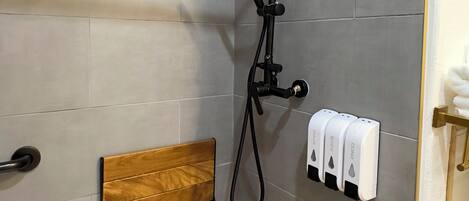 A shower area with a wooden bench, a handheld showerhead, and a towel dispenser.