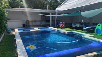 A swimming pool with a white tent overhead, surrounded by grass and trees.