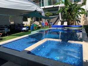 A swimming pool with two separate sections, surrounded by lounge chairs and a tent.