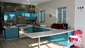 Een moderne keuken met blauwgroene kastjes, een roestvrijstalen fornuis en een rode magnetron.